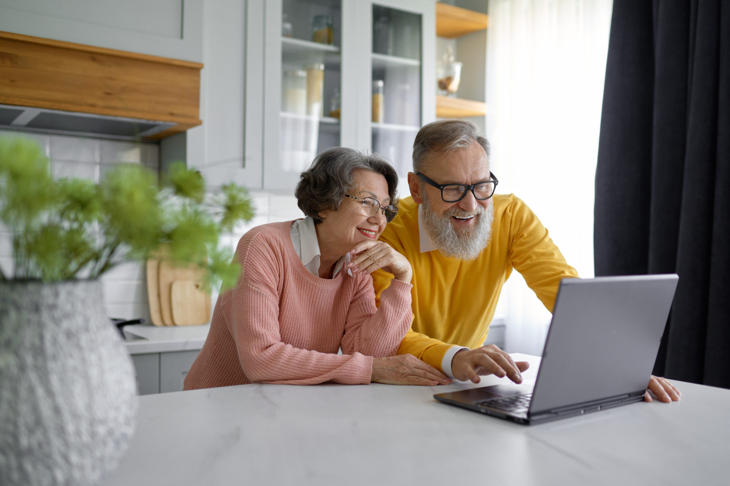 Retired family couple browsing internet using laptop at home kitchen